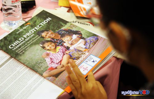 ស្ត្រីម្នាក់អង្គុយកាន់សៀវភៅរបាយការណ៍របស់អង្គការទស្សៈពិភពលោក (World Vision) ដែលមានចំណងជើងថា "Child Protection Learning Repoort 2018-2021" ថ្ងៃទី១០ ខែមិថុនា ឆ្នាំ២០២២។