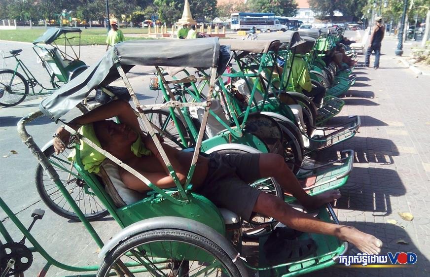 បុរសម្នាក់សម្រាករងចាំអតិថិជននៅលើស៊ីក្លូរបស់គាត់ក្បែរព្រះបរមរាជវាំង (ដោយ ទូច សុខា)