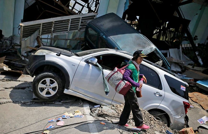 A woman walks past the wreckage of cars which was flattened by Friday's earthquake in Balaroa neighborhood in Palu, Central Sulawesi, Indonesia Indonesia, Tuesday, Oct. 2, 2018. (Dita Alangkara/AP)