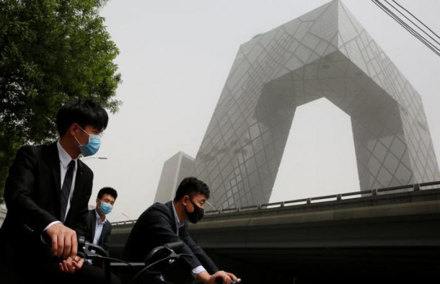People wear face masks as they wait to cross a street near the CCTV headquarters during a dust storm in Beijing