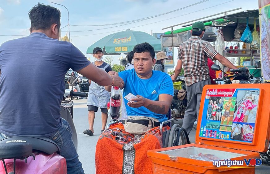 អតីតកីឡាករប្រដាល់ ធី ដារ៉ាម៉ា កំពុងអង្គុយលើរទេះលក់ទឹក និងភេសជ្ជៈ នៅតាមបណ្ដិយផ្លូវមាត់ទន្លេ នាក្រុងតាខ្មៅ ថ្ងៃទី១៤ ខែមករា ឆ្នាំ២០២៣។