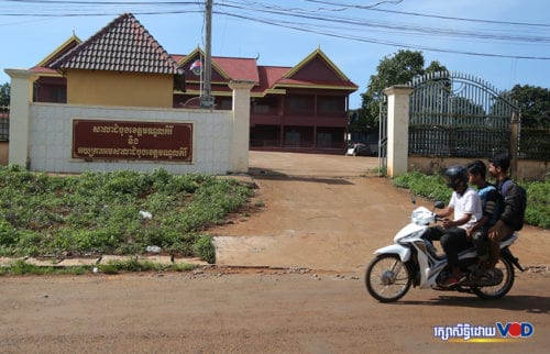 បុរសបីនាក់ជិះម៉ូតូតាមដងផ្លូវកាត់ពីមុខសាលាដំបូងខេត្តមណ្ឌលគិរី។